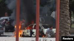 Warga di Benghazi berlindung di dekat mobil yang terbakar saat terjadi bentrokan hebat antara tentara Libya dan anggota kelompok Islamis Ansar al-Sharia di Benghazi, Libya, Senin (25/11). 