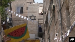 Jevrejske djevojke gledaju Izraelce i Palestince kako drže slike lubenice, palestinskog simbola, dok protestuju zbog iseljenja palestinske porodice od strane jevrejske naseljeničke organizacije ispred njihove kuće u muslimanskoj četvrti Starog grada Jerusalema, 16. juna 2023.