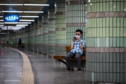 FILE - A commuter checks his phone as he sits in a train station of the Seoul Metropolitan Subway in Seoul, on August 24, 2021.