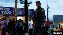 FILE - An army soldier patrols on a street next to people from Venezuela after checking their passports or identity cards at the Pacaraima border control, Roraima state, Brazil, Aug. 19, 2018. 