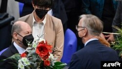 জার্মানির মনোনীত চ্যান্সেলর ওলাফ শোলজকে ফুল দিয়ে শুভেচ্ছা জানাচ্ছেন সংসদীয় দলের সকারী নেতা। (ফটো- এএফপি) 