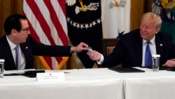 President Donald Trump smiles as Treasury Secretary Steven Mnuchin hands him a debit card that will be used to send payments by the Treasury Department to Americans during a Cabinet Meeting in the East Room of the White House, May 19, 2020.