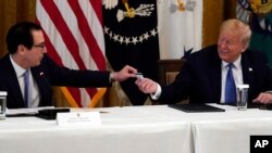President Donald Trump smiles as Treasury Secretary Steven Mnuchin hands him a debit card that will be used to send payments by the Treasury Department to Americans during a Cabinet Meeting in the East Room of the White House, May 19, 2020.