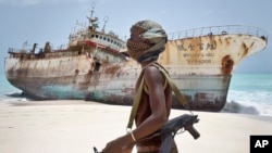 FILE - Masked Somali pirate walks past a fishing vessel.