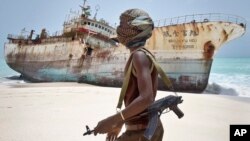 FILE - Masked Somali pirate walks past a fishing vessel.