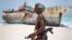 FILE - Masked Somali pirate walks past a fishing vessel.