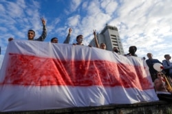 People hold a handmade banner of an old Belarusian national flag as they gather to protest results of the country's presidential election in Minsk, Belarus, Aug. 13, 2020.