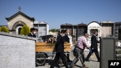 Workers of a funeral home company pull the coffin of a COVID-19 victim for burial at the cemetery near Cuneo, northwestern Italy, April 24, 2020.