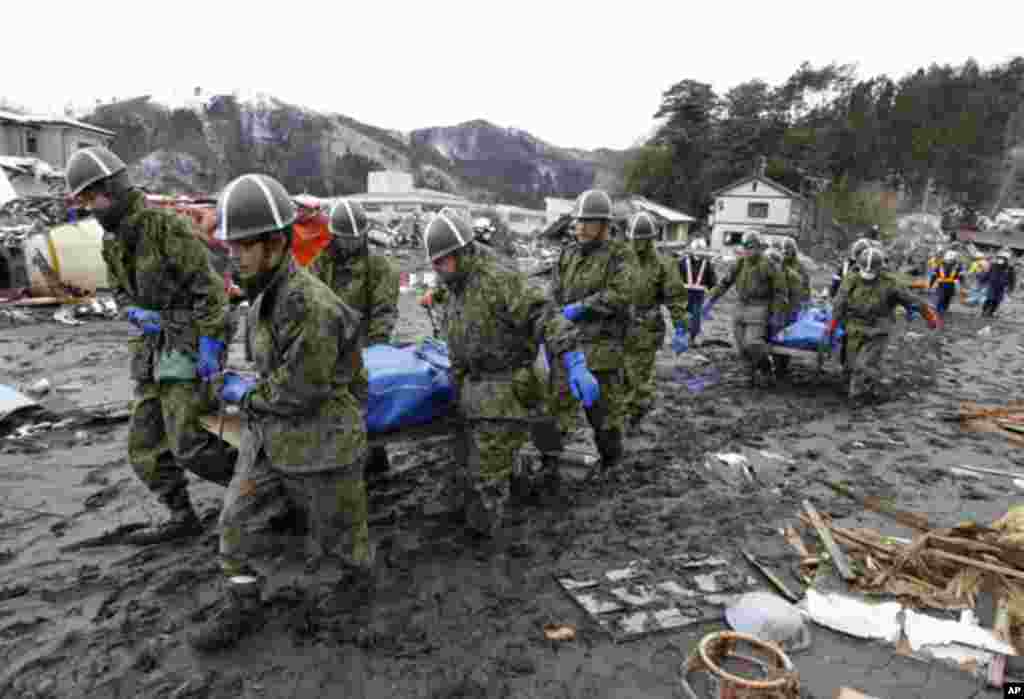 Japanese military personnel carry bodies of victims at a village destroyed by earthquake and tsunami in Yamadamachi. (Reuters Image)