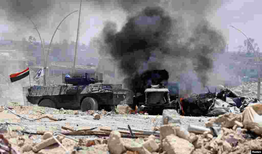 An Iraqi military armored fighting vehicle drives past a burning military truck after it was hit by the Islamic State militants during fighting in western Mosul.