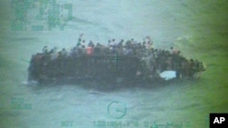 This image taken from video made available by the U.S. Coast Guard shows a group of Haitian migrants sitting on the hull of a capsized sailboat. Nov. 26, 2013, (AP Photo/U.S. Coast Guard)