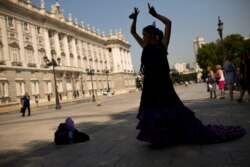 FILE - A street artist wearing a flamenco dress performs in front of the Royal Palace in Madrid, Sept. 8, 2017.