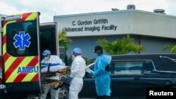 Un enfermo de coronavirus en Miami llega en ambulancia a un hospital especializado, mientras otro es sacado en un carro fúnebre.