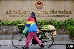 Esta fotografía tomada el 5 de febrero de 2025 muestra a una vendedora de frutas caminando frente al Ministerio de Información y Comunicaciones en Hanoi.