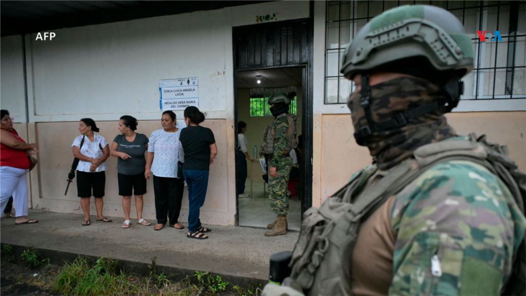 Personal militar hace guardia mientras las mujeres hacen fila para votar en un colegio electoral en Canuto, Ecuador, el 9 de febrero de 2025, durante las elecciones presidenciales.