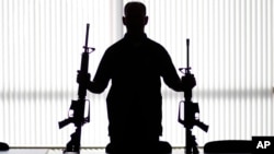 FILE - An agent of the U.S. Bureau of Alcohol, Tobacco, Firearms and Explosives holds guns at an ATF field office in Glendale, California, Aug. 9, 2017.