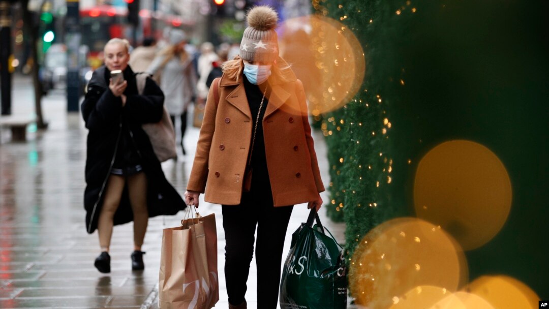 Seorang perempuan, yang mengenakan masker untuk menjaga diri dari infeksi COVID-19, membawa beberapa kantong belanjaan ketika berjalan melalui Oxford Street di London, pada 27 Desember 2021. (Foto: AP/David Cliff)