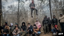 TOPSHOT - Migrants sit waiting near the buffer zone at Turkey-Greece border, at Pazarkule, in Edirne district, on February 29, 2020. - Thousands of migrants stuck on the Turkey-Greece border clashed with Greek police on February 29, 2020, according…