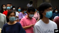 Parents and relatives wearing face masks to protect against the coronavirus wait for students to finish taking national college entrance exams on the final day of testing in China, July 10, 2020, in Beijing.