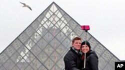 Sepasang turis AS mengambil swafoto di depan Piramida Louvre, Paris. (AP/Remy de la Mauviniere)