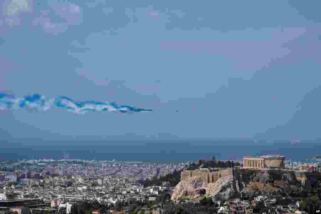 Alpha jets from the Patrouille de France team and two French Air Force Rafale jets spray lines of smoke in the colors of the Greek flag as they fly past the Parthenon Temple atop the Acropolis hill, Greece.