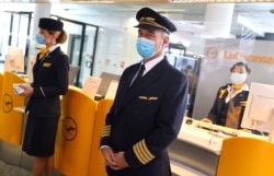 FILE - Employees of German airline Lufthansa wear protective masks as they wait for passengers at a boarding gate at the airport in Frankfurt, Germany, June 17, 2020.
