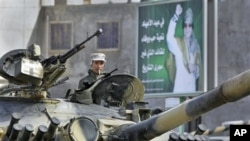 A Libyan army soldier loyal to Libyan leader Moammar Gadhafi, on poster in background, sits in a tank, in Qasr Banashir, southeast of the capital Tripoli, March 1, 2011