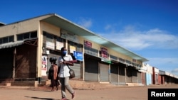 FILE - A man wears a mask as he walks past closed shops during a lockdown aimed at limiting the spread of the coronavirus disease (COVID-19) in Harare, Zimbabwe, Jan. 28, 2021.