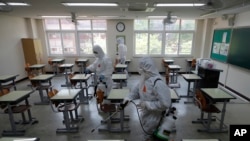 Health officials wearing protective gear spray disinfectant to help reduce the spread of the new coronavirus in a class at a high school in Seoul, South Korea, May 11, 2020.