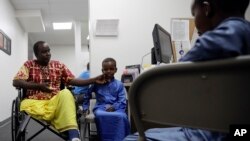 FILE - Ali Said, of Somalia, left, waits at a center for refugees with his two sons, July 6, 2017, in San Diego. Said, whose leg was blown off by a grenade, says he felt unbelievably lucky to be among the last refugees allowed into the United States befor