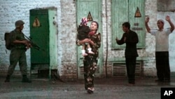 FILE - A resident with a child walks by a soldier during an uprising in Andijan, Uzbekistan, May 13, 2005. A rare protest by crowds in Babur Square who were demanding an end to corruption and injustice ended with hundreds dead in torrents of blood.