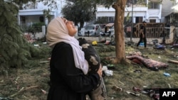 A woman reacts while holding a pillow as she stands amid debris outside the site of the Ahli Arab hospital in central Gaza on Oct. 18, 2023, in the aftermath of an overnight strike there. Israeli and Gazan officials blame each other for the blast, which killed hundreds of people.