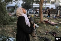 Seorang perempuan tersedu sambil memegang bantal saat berdiri di tengah puing-puing di luar lokasi rumah sakit Ahli Arab di Gaza tengah pada 18 Oktober 2023 setelah serangan semalaman di sana. (Foto: AFP)