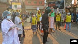 ຊາຍຄົນນຶ່ງຈາກອົງການບໍ່ຂຶ້ນກັບລັດຖະບານ ຫຼື NGO ໃສ່ຊຸດທີ່ຄ້າຍຄືກັບ ພະຍາດໂຄວິດ-19 ຫຼື ໄວຣັສໂຄໂຣນາ ເຄື່ອນຍ້າຍໄປທົ່ວຕະຫຼາດ ເພື່ອຮຽກຮ້ອງໃຫ້ປະຊາຊົນປະຕິບັດຕາມ ກົດລະບຽບໃນການຮັກສາຄວາມປອດໄພ ໃນລະຫວ່າງການປຸກລະດົມ ໃຫ້ຕື່ນຕົວ ທີ່ຈັດຂຶ້ນຢູ່ໃນເມືອງຊີລີກູຣີ ຂອງອິນເດຍ, ວັນທີ 25 ເມສາມ 2021. 