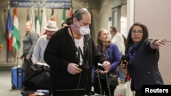 FILE - A ticket agent helps travelers arriving on a flight from Frankfurt, Germany before travel restrictions were enacted hours later on flights from Europe at the Denver International Airport, March 13, 2020. 