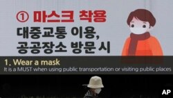 Una mujer que usa una máscara facial pasa por una pantalla en la plaza Dongdaemun Design, en Seúl, Corea del Sur, que muestra las precauciones que se deben tomar para prevenir el coronavirus. Abril 19 de 2020.