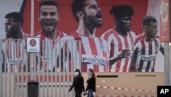 Two women wearing face masks pass by a giant poster of Atletico Madrid soccer players at the Wanda Metropolitano stadium in Madrid, Spain, May 5, 2020. 