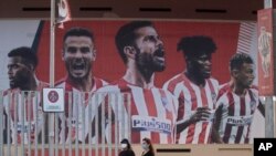 Two women wearing face masks pass by a giant poster of Atletico Madrid soccer players at the Wanda Metropolitano stadium in Madrid, Spain, May 5, 2020. 