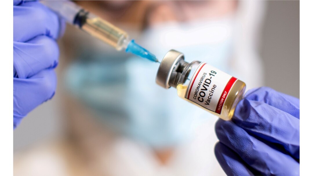 A woman holds a small bottle labeled with a "Coronavirus COVID-19 Vaccine" sticker and a medical syringe in this illustration taken Oct. 19, 2020.