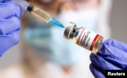 A woman holds a small bottle labeled with a "Coronavirus COVID-19 Vaccine" sticker and a medical syringe in this illustration taken Oct. 19, 2020.