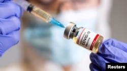 A woman holds a small bottle labeled with a "Coronavirus COVID-19 Vaccine" sticker and a medical syringe in this illustration taken Oct. 19, 2020.