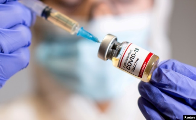 A woman holds a small bottle labeled with a "Coronavirus COVID-19 Vaccine" sticker and a medical syringe in this illustration taken Oct. 19, 2020.