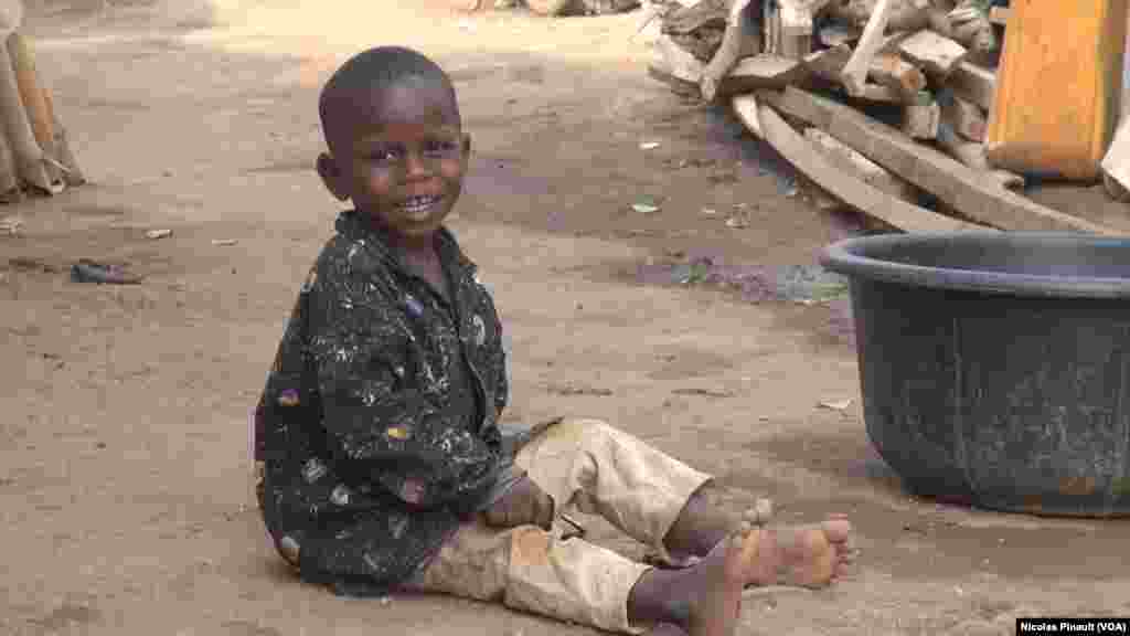 Un enfant regarde sa mère faire la lessive, dans le camp de déplacés de New Kuchogoro, à Abuja, le 7 mars 2016. (VOA/Nicolas Pinault)