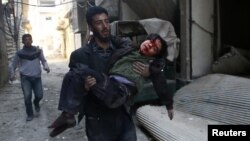 Seorang pria membopong anak laki-laki yang terluka di Kota Hamouriyeh, yang dikuasai dan dan dikepung pemberontak di timur Ghouta, dekat Damascus, Suriah, 21 Februari 2018.