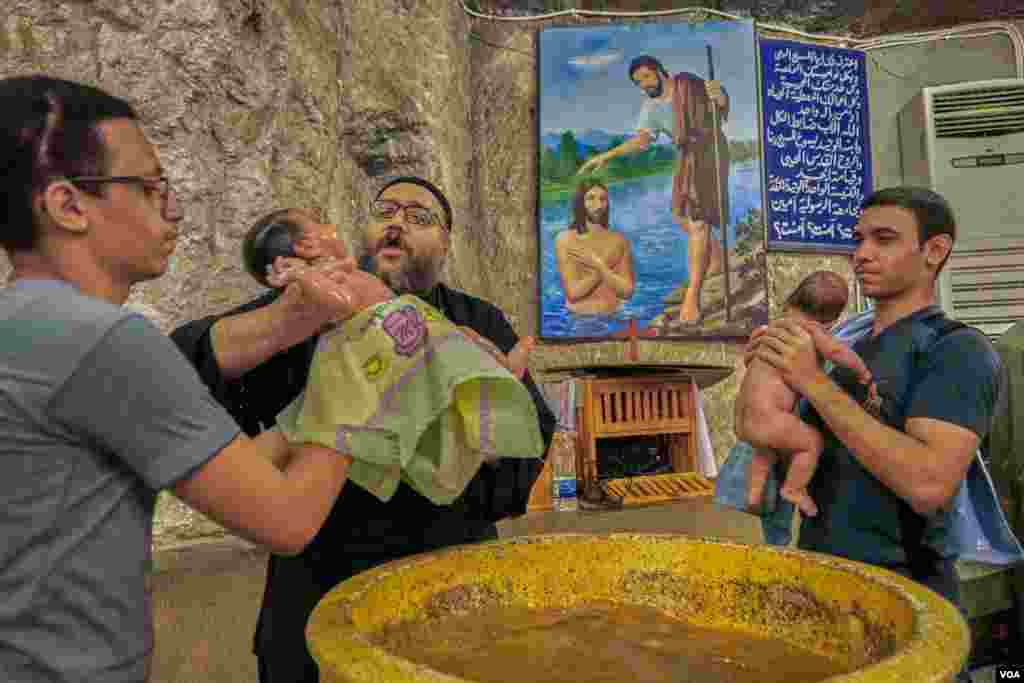 A priest in the monastery of Virgin Mary is baptizing small children during a ceremony while parents are filming the process. Sunday, August 18, 2019.