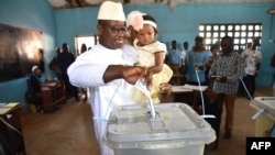 Sierra Leone's People Party presidential candidate Julius Mada Bio holds his daughter while casting his ballot for the general elections, at a polling station in Freetown, March 7, 2018, as his wife looks on.