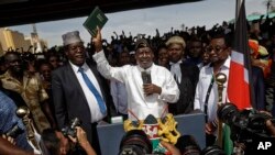 FILE - Opposition leader Raila Odinga, center, accompanied by lawyer Miguna Miguna, center-left, and others, holds a Bible aloft after a mock "swearing-in" ceremony at Uhuru Park in downtown Nairobi, Kenya, Jan. 30, 2018.