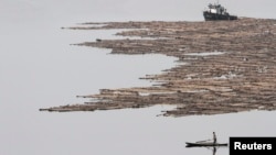 FILE - A North Korean man rows a boat past logs, which were tied together and transported by boats on the Yalu River near the North Korean city of Hyesan, Aug. 16, 2014.