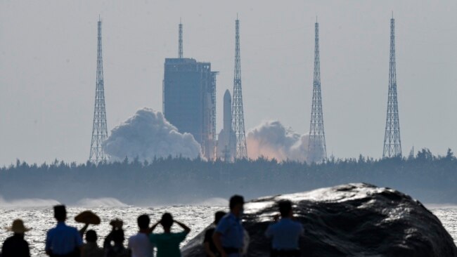 In this photo released by Xinhua News Agency, people watch the Long March-5B Y4 carrier rocket carrying the space lab module Mengtian, blasts off from the Wenchang Satellite Launch Center in south China's Hainan Province, Monday, Oct. 31, 2022.