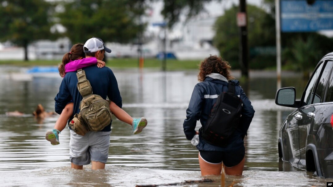 Don Noel carries his daughter Alexis, 8, with his wife Lauren, right as they walk through a flooded roadway to check on their boat in the West End section of New Orleans, June 21, 2017.